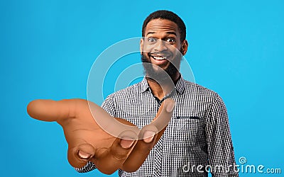 Surprised young black man standing with big outstretched hand on blue studio background, mockup for your product Stock Photo