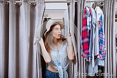 Surprised young woman looking out of dressing room Stock Photo