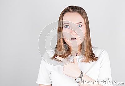 Surprised young woman points her finger to the space to her left. Portrait of a surprised girl on a gray background Stock Photo