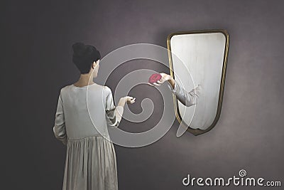 Surreal gesture of a hand coming out of the mirror to give a rose to a woman Stock Photo