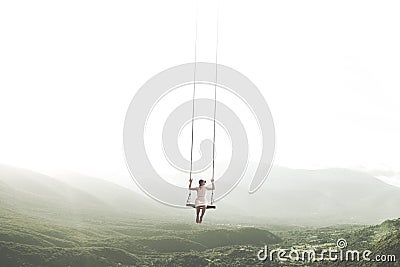 Surreal moment of a woman having fun on a swing hanging from the sky Stock Photo