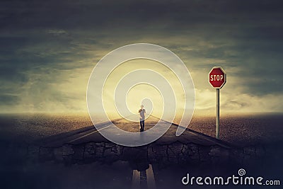 Surreal view as man walks a crushing asphalt road as STOP red sign warns of danger. Deep hole in the ground, chasm as broken way Stock Photo