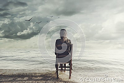 Surreal woman looks at the infinite sitting on a chair inside the sea Stock Photo
