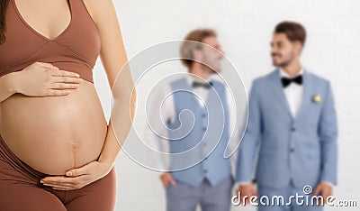 Surrogacy concept. Young pregnant woman and blurred view of happy gay couple on light background Stock Photo