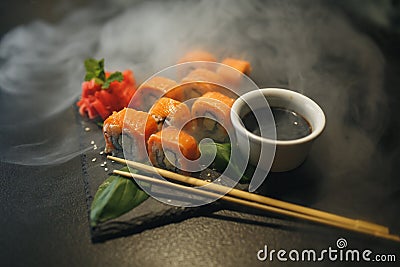 Sushi roll with cream cheese and fried salmon. Being picked up with chopsticks from soy sauce, with more rolls on black Stock Photo
