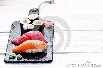 Sushi set served on a black slate. Sushi rolls and sashimi on a wooden white table. Seafood. Raw fish. White background. Wasabi. Stock Photo