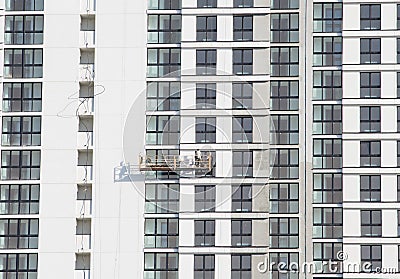 Suspended cradle on the facade of the skyscraper. Mobile scaffolding platform for construction work at height, facade cleaning, Stock Photo
