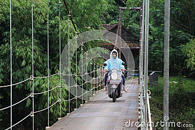 Suspension bridge over the river with motorcycle crossing on it in the morning in Sukabumi, west java, Indonesia. traditional Editorial Stock Photo