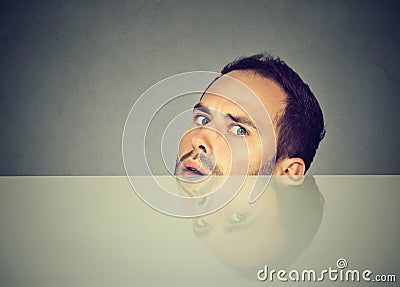 Suspicious scared man peeking from under the table hiding Stock Photo