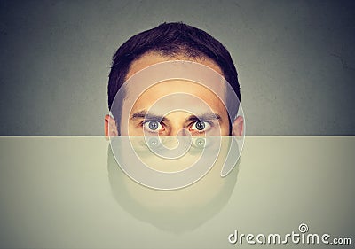 Suspicious scared man peeking from under the table hiding Stock Photo