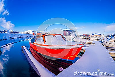 SVOLVAER, LOFOTEN ISLANDS, NORWAY - APRIL 10, 2018: View of fishing boats covered with snow in harbour with buildings in Editorial Stock Photo