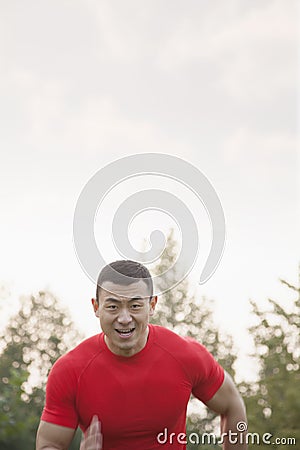 Sweating, tired, muscular man with a red shirt running toward camera in a park in Beijing, China Stock Photo