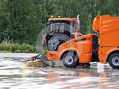 The sweeping machine rides through the park and cleans the sidewalk. City background with sweeper Stock Photo