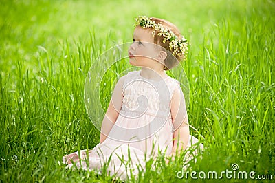 Sweet baby girl in wreath of flowers sitting on green grass Stock Photo