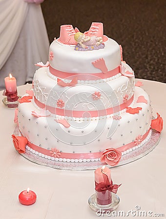 Sweet baptize cake with pink sugar shoes and burning candles Stock Photo