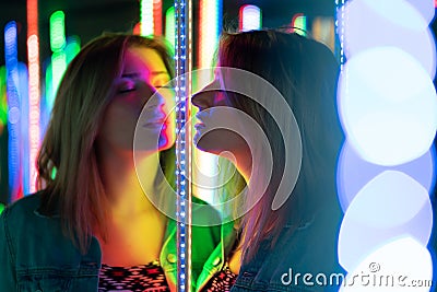 Sweet caucasian girl walks in a mirror maze with colorful diodes and enjoys an unusual attraction room in the city Stock Photo