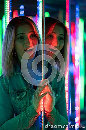 Sweet caucasian girl walks in a mirror maze with colorful diodes and enjoys an unusual attraction room in the city Stock Photo