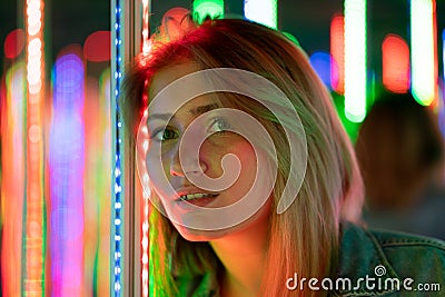 Sweet caucasian girl walks in a mirror maze with colorful diodes and enjoys an unusual attraction room in the city Stock Photo