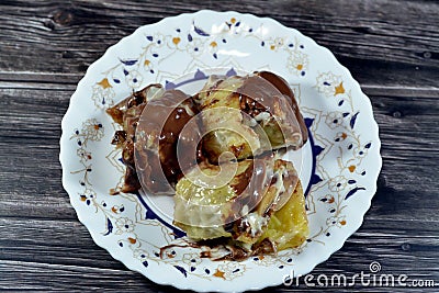 Sweet chocolate mix rolls stuffed with banana fruit pieces, nuts, hazelnuts, raisins, white and brown chocolate sauce with topping Stock Photo