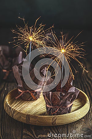 Sweet chocolate muffins with sparklers in brown paper with ribbon on wooden bowl. Close up, shallow depth of the field, greeting Stock Photo