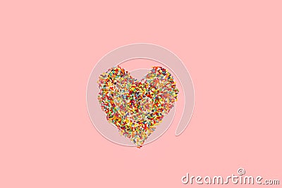 Sweet colored sprinkles in heart shape on a pink background Stock Photo