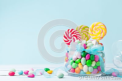 Sweet colorful candy in jar decorated with bow ribbon against blue background. Gifts for Birthday party. Stock Photo