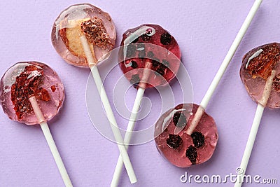 Sweet colorful lollipops with berries on lilac background, flat lay Editorial Stock Photo