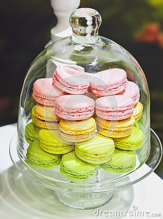 Sweet and colourful french macaroons or macaron in a glass bell jar or glass tray on a white wooden table. Dessert. Can be used fo Stock Photo