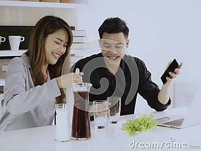 Sweet couples are eating breakfast together in office room. there are red juice and green vegetable salad roll on their table with Editorial Stock Photo