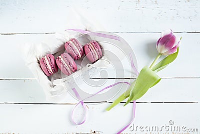 Sweet crimson french macaroons with box and tulip on light dyed wooden background Stock Photo