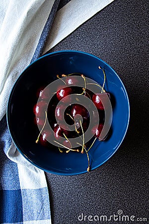 Sweet dark cherries in a ceramic bowl on a dark background and kitchen towel with a line. Top view Stock Photo