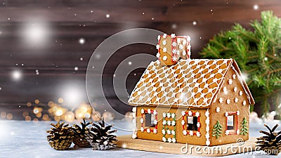 Sweet decorated gingerbread house closeup with pine cones decorations, fir tree branches, bokeh and snowfall. Christmas card with Stock Photo