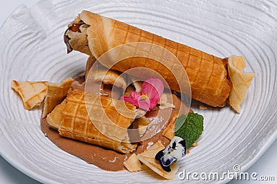 Sweet dessert. Wafer tubules with a delicate protein cream and a small sieve with powdered sugar on a white round tray Stock Photo