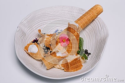 Sweet dessert. Wafer tubules with a delicate protein cream and a small sieve with powdered sugar on a white round tray Stock Photo