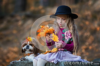 Sweet girl in a hat weaves wreath of autumn maple leaves Stock Photo