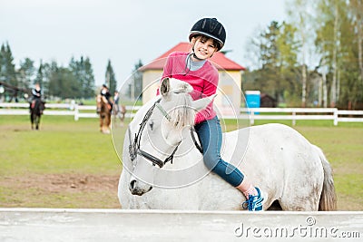 A sweet girl riding a white horse, an athlete engaged in equestrian sports, a girl hugs and kisses a horse. Stock Photo