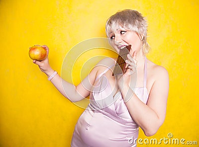 Sweet joyous curvaceous girl with a short haircut stands in a delicate evening silk dress and compares bad and good food Stock Photo