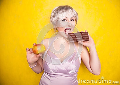 Sweet joyous curvaceous girl with a short haircut stands in a delicate evening silk dress and compares bad and good food Stock Photo