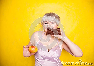 Sweet joyous curvaceous girl with a short haircut stands in a delicate evening silk dress and compares bad and good food Stock Photo