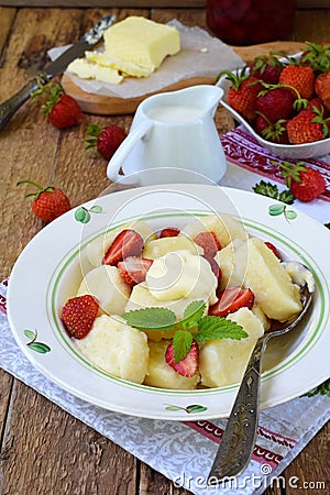 Sweet lazy pierogi. Ukrainian dumplings with sour cream, butter and strawberry on wooden background. Summer berry breakfast. Stock Photo