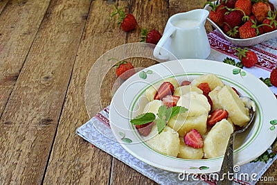 Sweet lazy pierogi. Ukrainian dumplings with sour cream, butter and strawberry on wooden background. Summer berry breakfast. Stock Photo