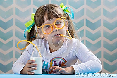 Sweet little girl drinking milk with funny glasses straw. Stock Photo