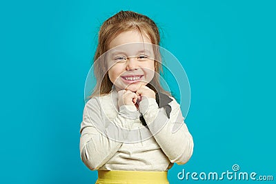 Sweet little girl has folded her hands under chin, smiles beautifully, anticipates an event or holiday, expresses Stock Photo