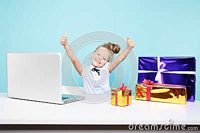 Sweet little girl siting at the desk with a lot of xmas gifts and the laptop. Stock Photo