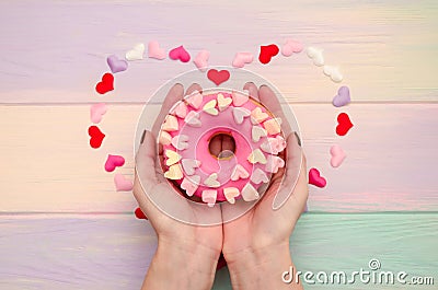 Sweet pink donut with icing and decoration with hearts on rainbow wooden background in female hands Stock Photo
