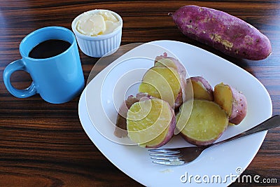 Sweet potato in a white plate with cup of black coffe, bowl of butter and raw potato. Stock Photo