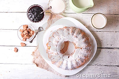 Sweet round fruity homemade pie with hole, on a white dish on a wooden table served with a cup of milk. Piece of cake Stock Photo