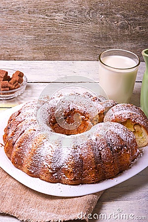 Sweet round fruity homemade pie with hole, on a white dish on a wooden table served with a cup of milk. Piece of cake Stock Photo