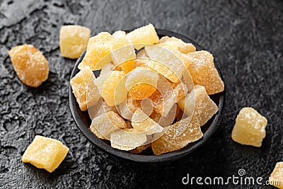 Sweet and spicy candied ginger in black bowl on dark stone background Stock Photo