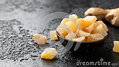 Sweet and spicy candied ginger in black bowl on dark stone background Stock Photo